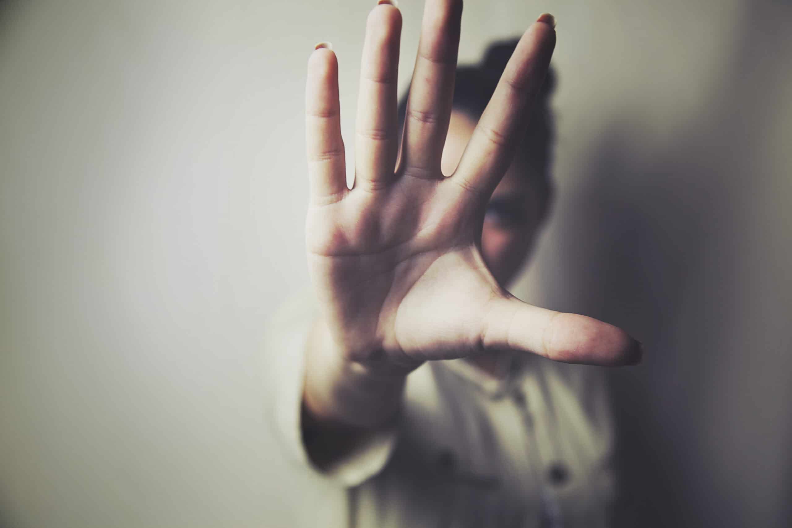 A person holds an open hand toward the camera, obscuring their face. The background is neutral and out of focus.