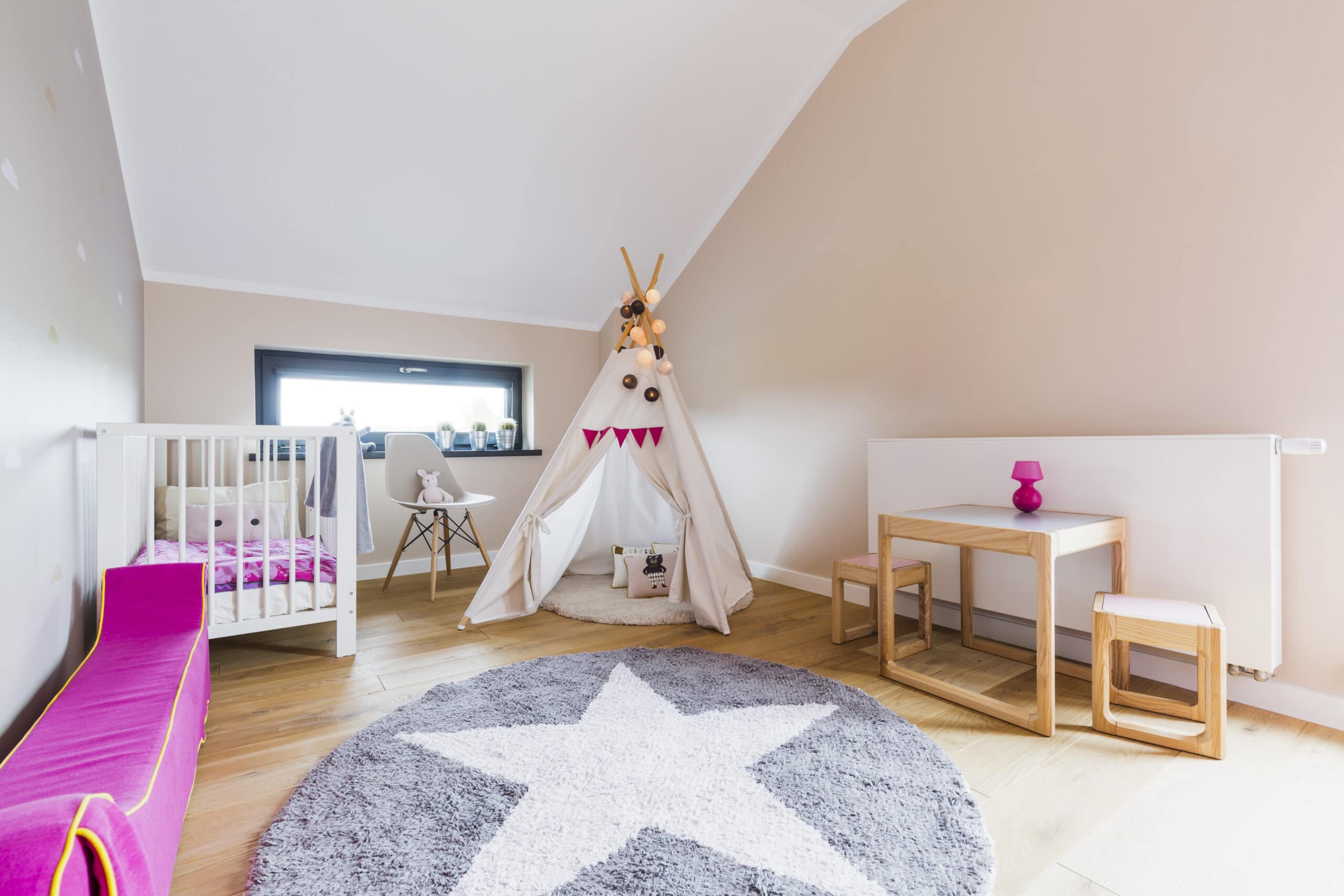 A children's room with a crib, a teepee tent, a small table with chairs, a pink bench, and a round rug with a white star pattern on a wooden floor.