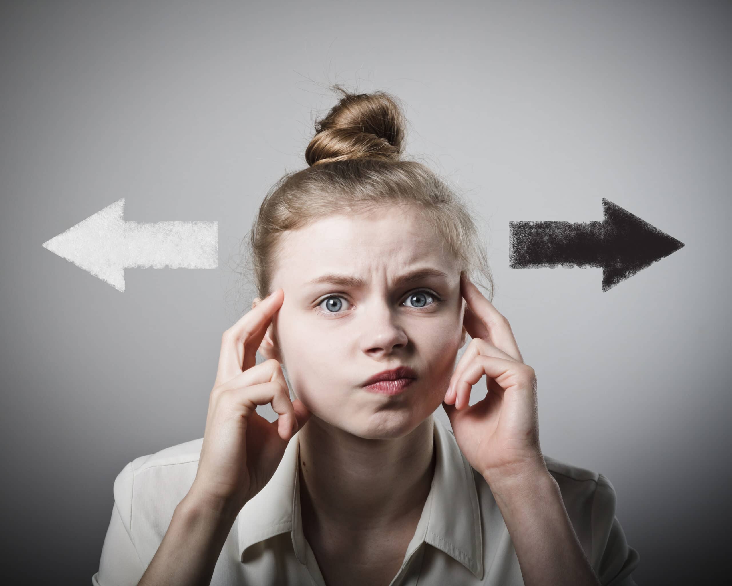 A young woman looks confused, touching her temples, with a white arrow pointing left and a black arrow pointing right drawn behind her on a gray background.