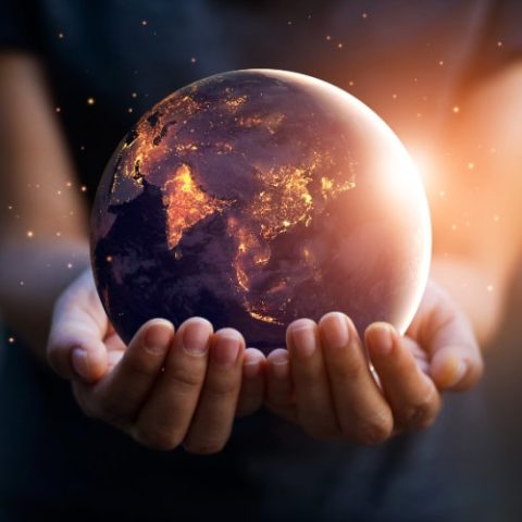 A person holds a glowing Earth in their hands, showing illuminated continents against a dark background.