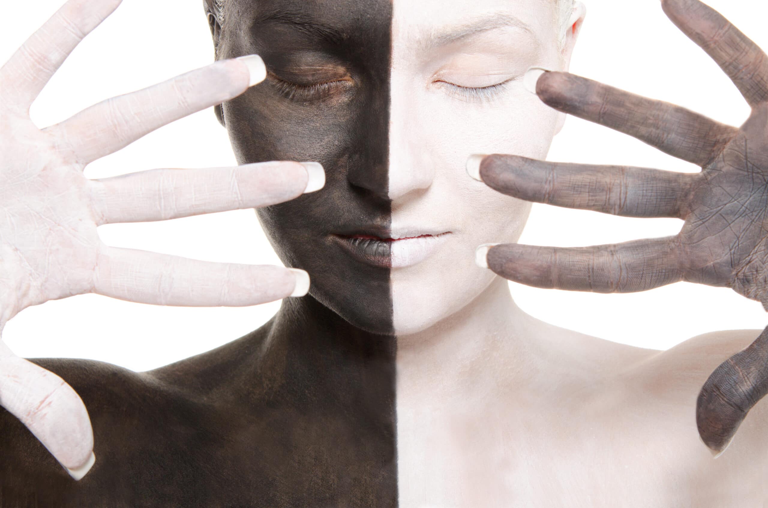 A person with their face and hands painted in stark black and white halves, eyes closed, holding their hands in front of their face against a white background.