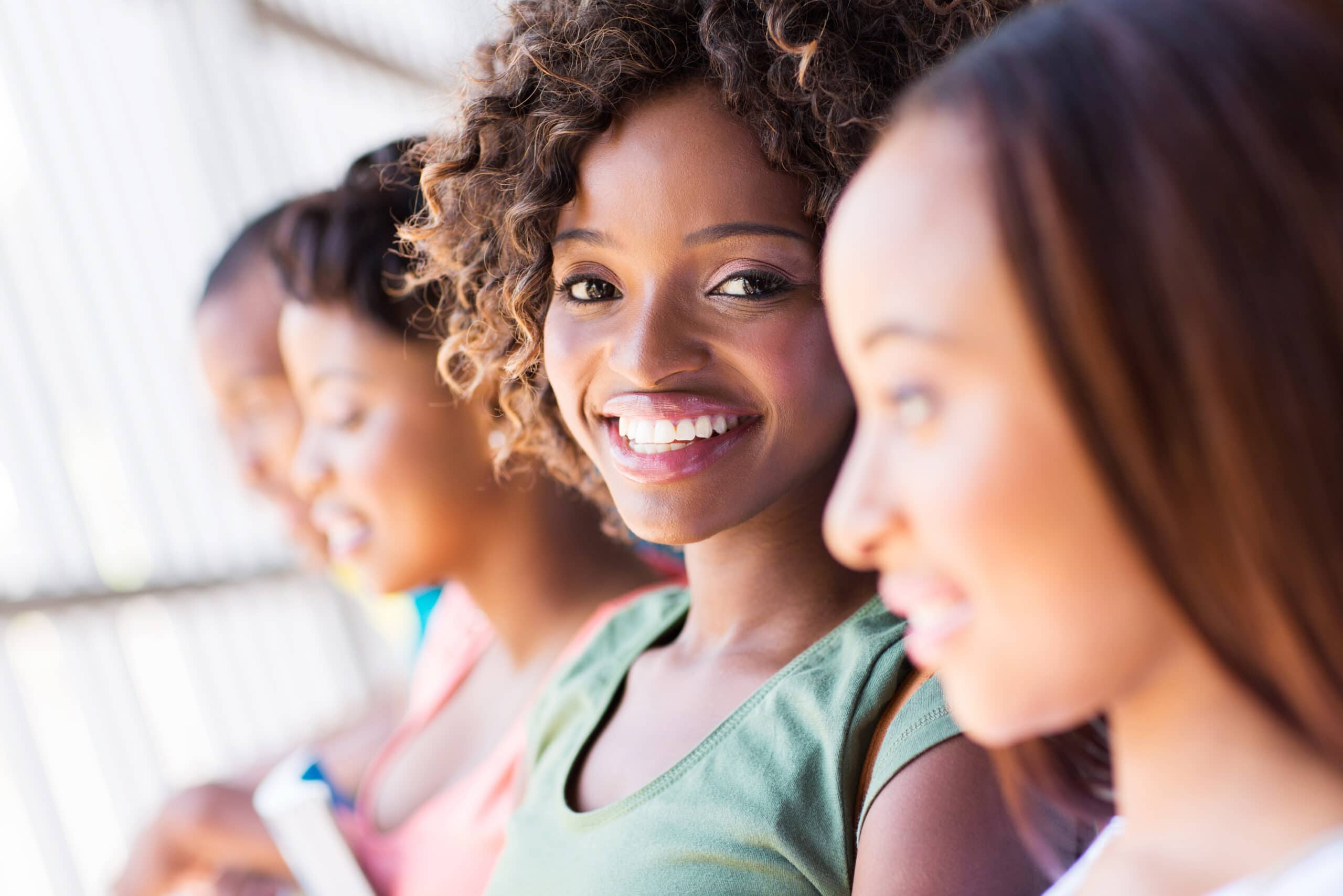 A young woman smiles at the camera while sitting in a row with three other women, who are slightly out of focus.