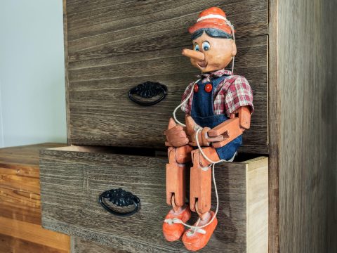 A wooden Pinocchio puppet sits on the edge of an open dresser drawer, with its legs dangling and hands tied with string.