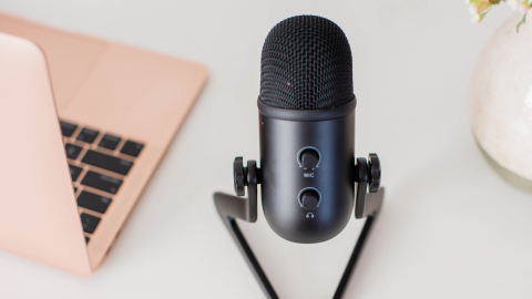Black USB microphone on a stand placed on a white desk next to a rose gold laptop—an ideal setup for an LDS Life Coach conducting virtual sessions or creating uplifting content.