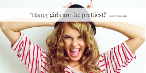 Young woman with long curly hair wearing a black hat and striped shirt smiles widely with hands on her head; quote overlay reads, "Happy girls are the prettiest!" by Audrey Hepburn.
