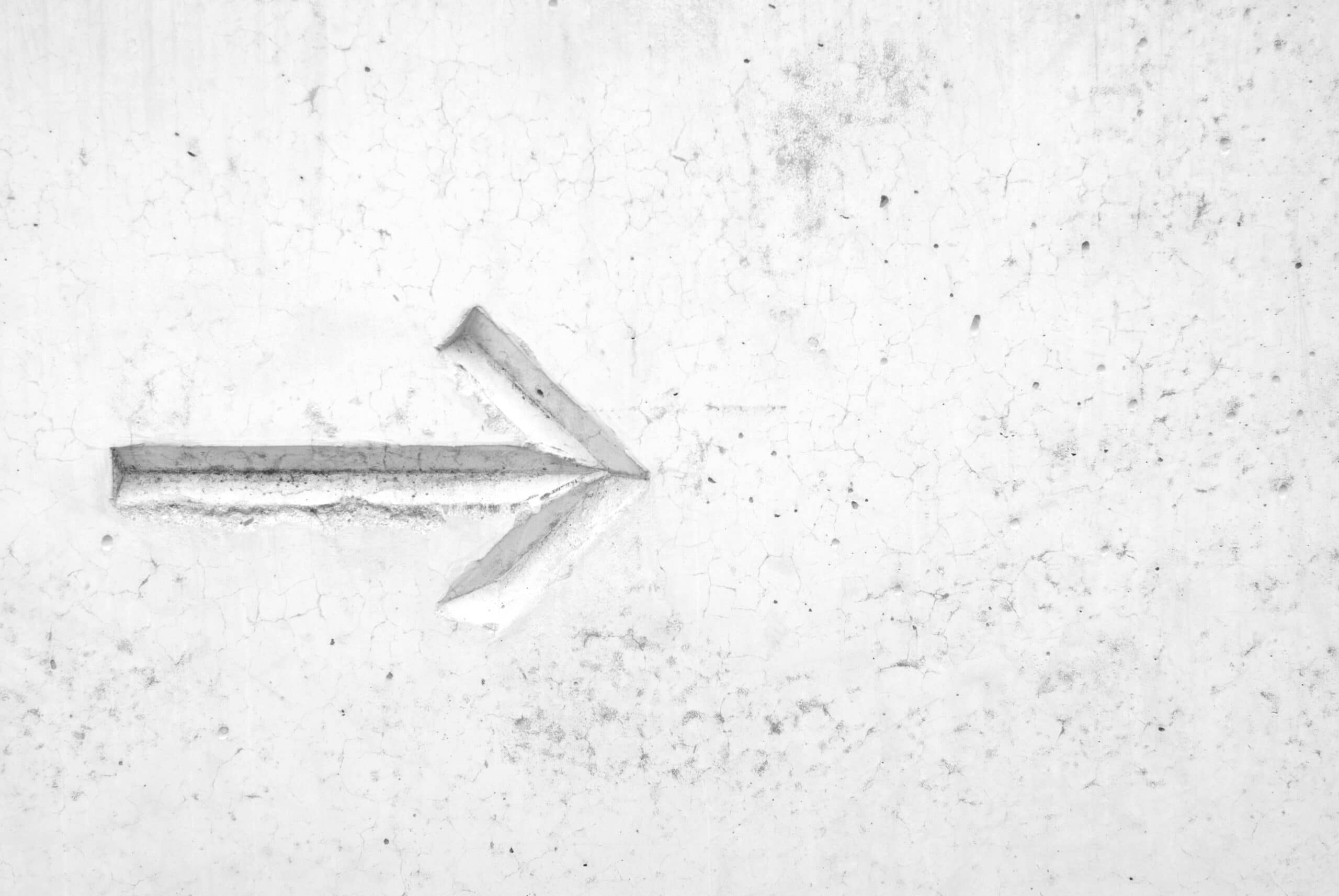 A right-pointing arrow is carved into a white, cracked concrete wall.