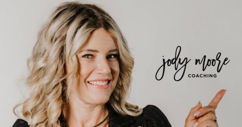 Smiling woman with blonde curled hair points at "jody moore coaching" text on a plain background.